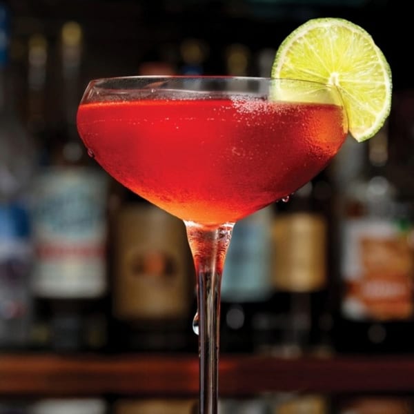 A vibrant red cocktail in a coupe glass, garnished with a fresh lime slice at il Mulino.