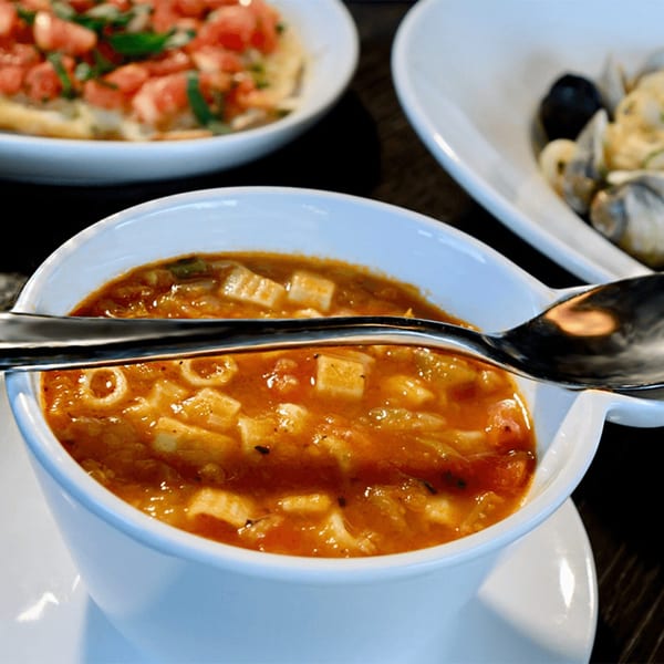 A bowl of Italian minestrone soup with pasta, alongside bruschetta and mussels.
