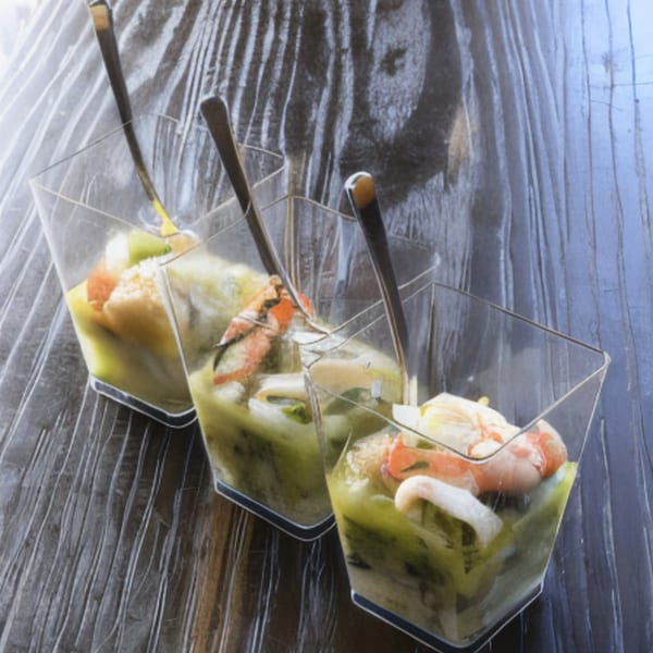 Three clear square glasses filled with green sauce, shrimp, and other seafood, with small spoons.