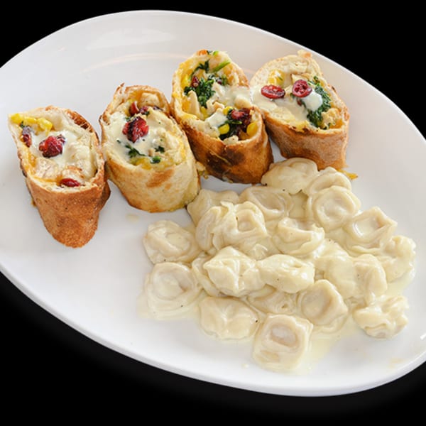 Four baked bread rolls with creamy filling and cranberries, next to a pile of tortellini in cream sauce.