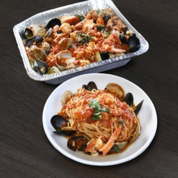il Mulino's seafood pasta with mussels, clams, and shrimp in a red sauce, served in a foil pan and on a white plate.