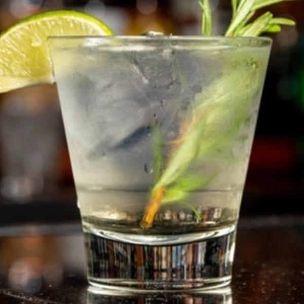 A refreshing il Mulino cocktail with a lime wedge and rosemary sprig in a glass.