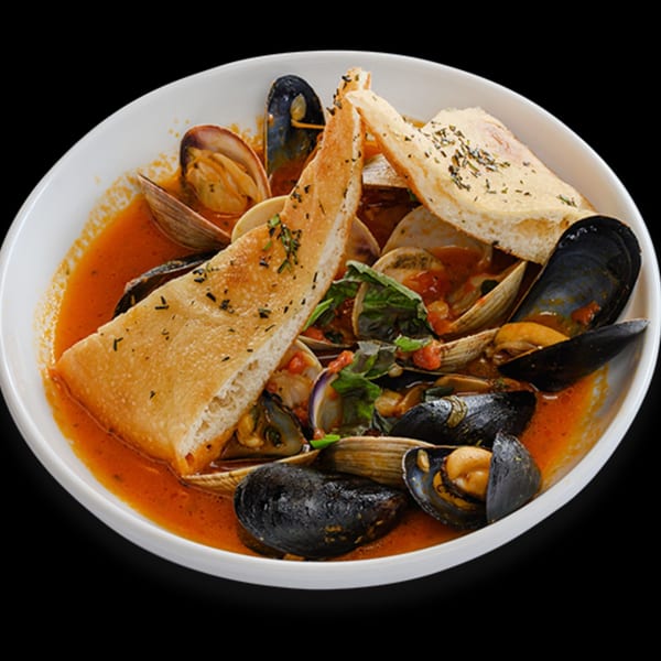 A white bowl of il Mulino's seafood stew with mussels, clams, and toasted bread.